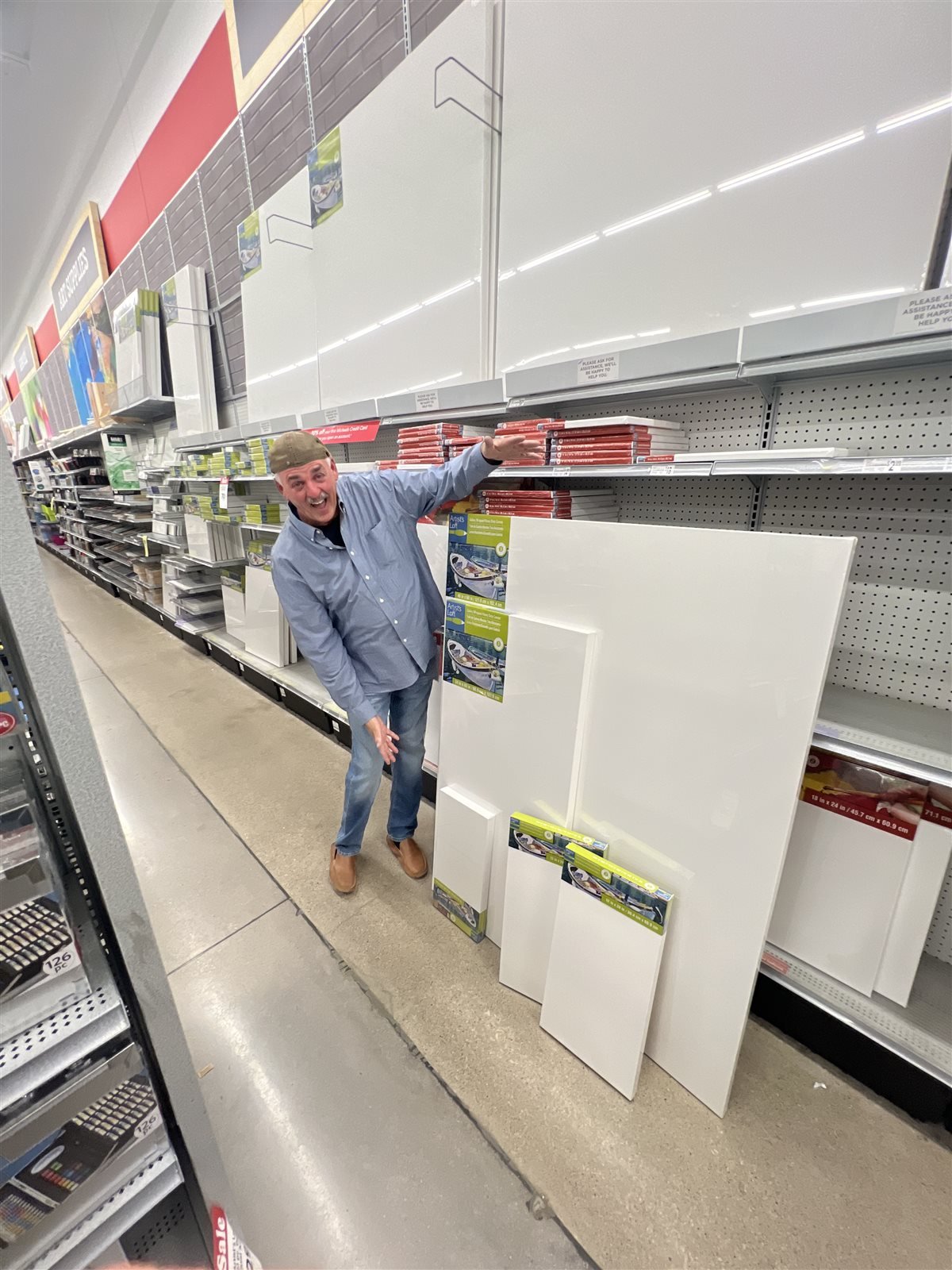Lee Adams smiling and reaching for blank canvases on a shelf at an art supply store.